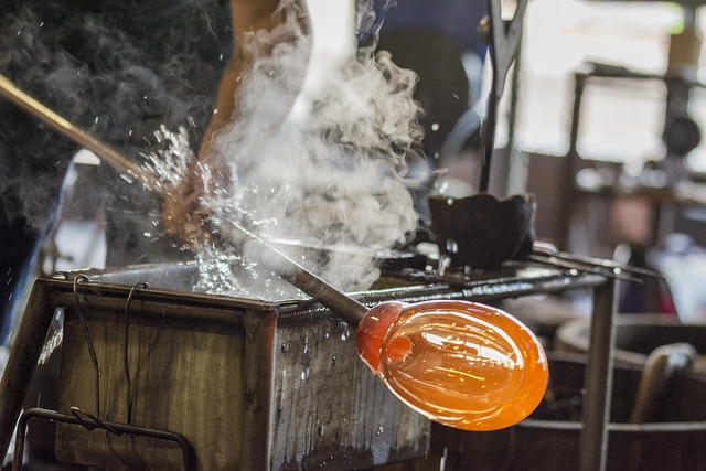 Glass artist blowing molten glass with steam rising
